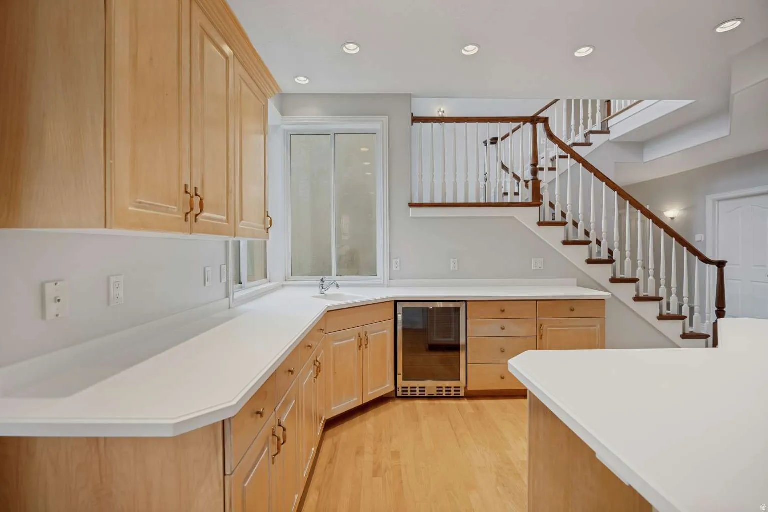 Wood-finish cabinetry with white countertops, integrated beverage cooler, and wood-finish flooring