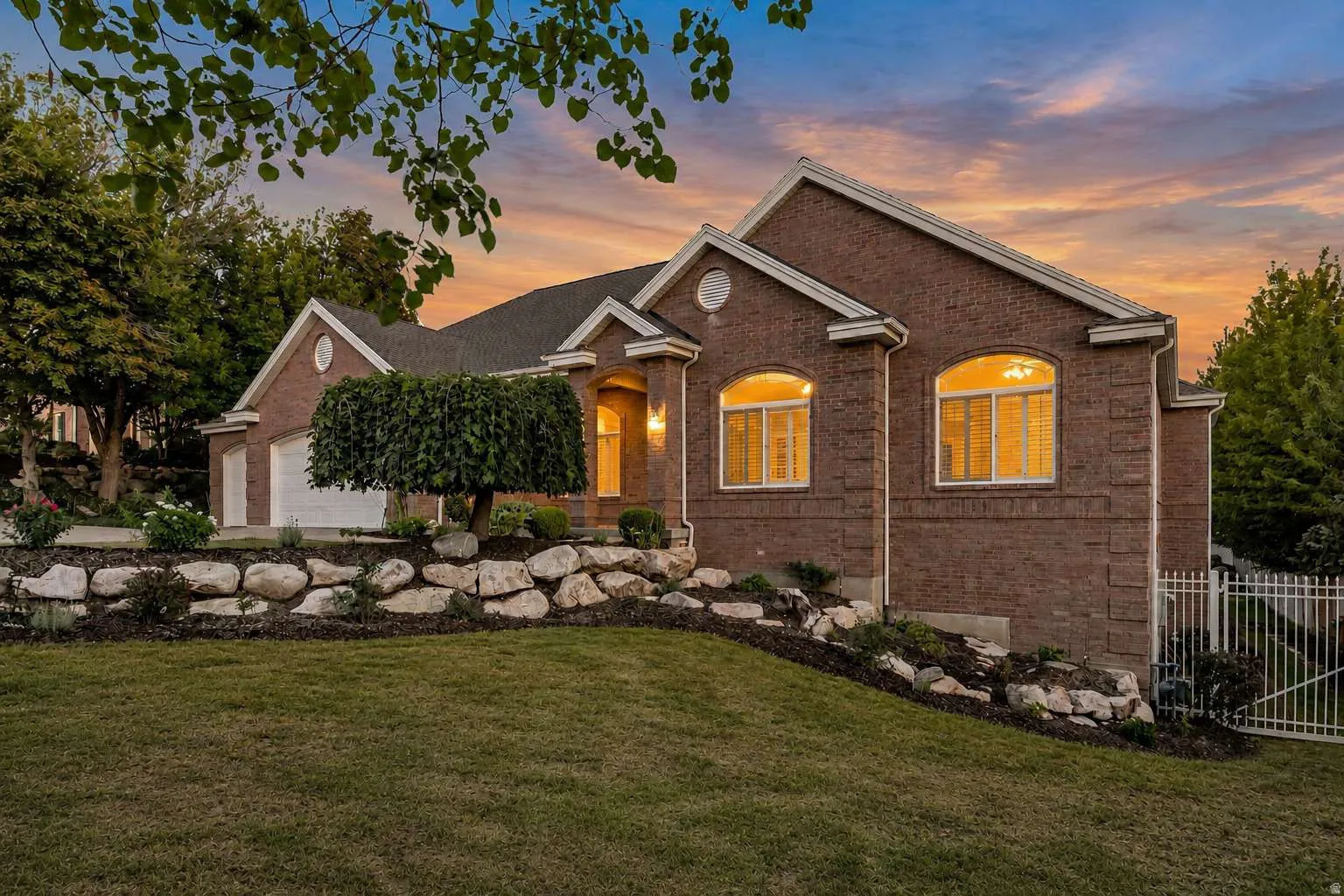 Brick exterior, arched windows, attached garage, metal fencing, and landscaped retaining wall