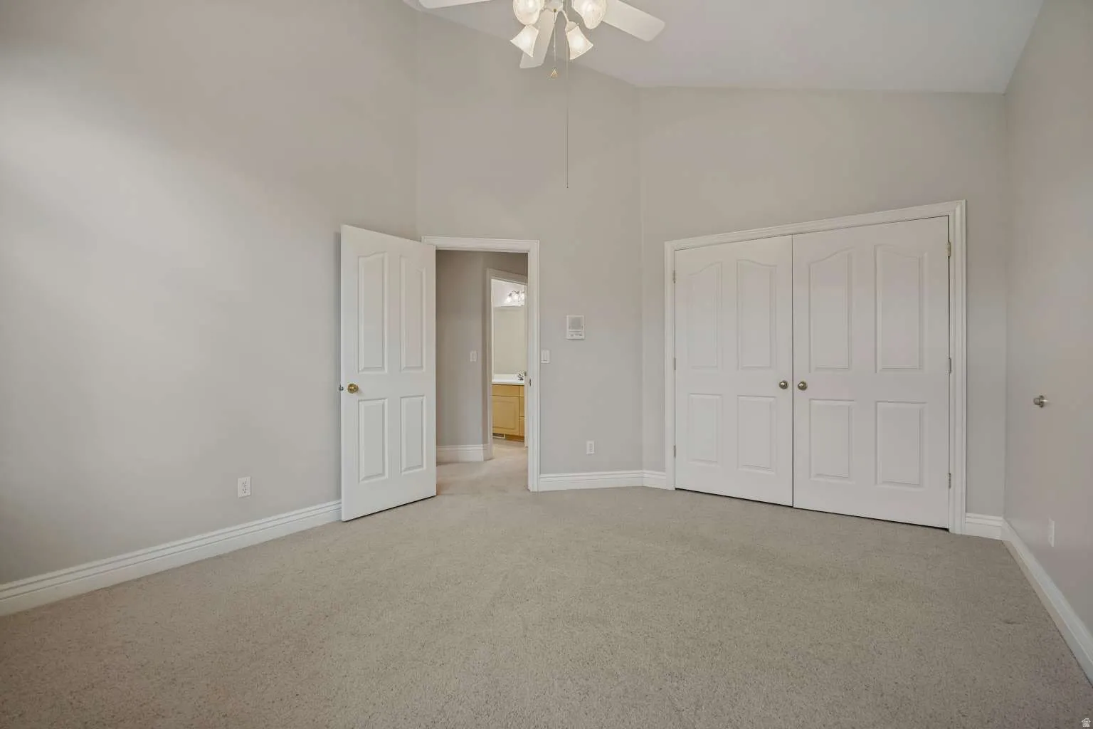 Vaulted ceiling with a ceiling fan, carpeted flooring, and bi-fold closet doors