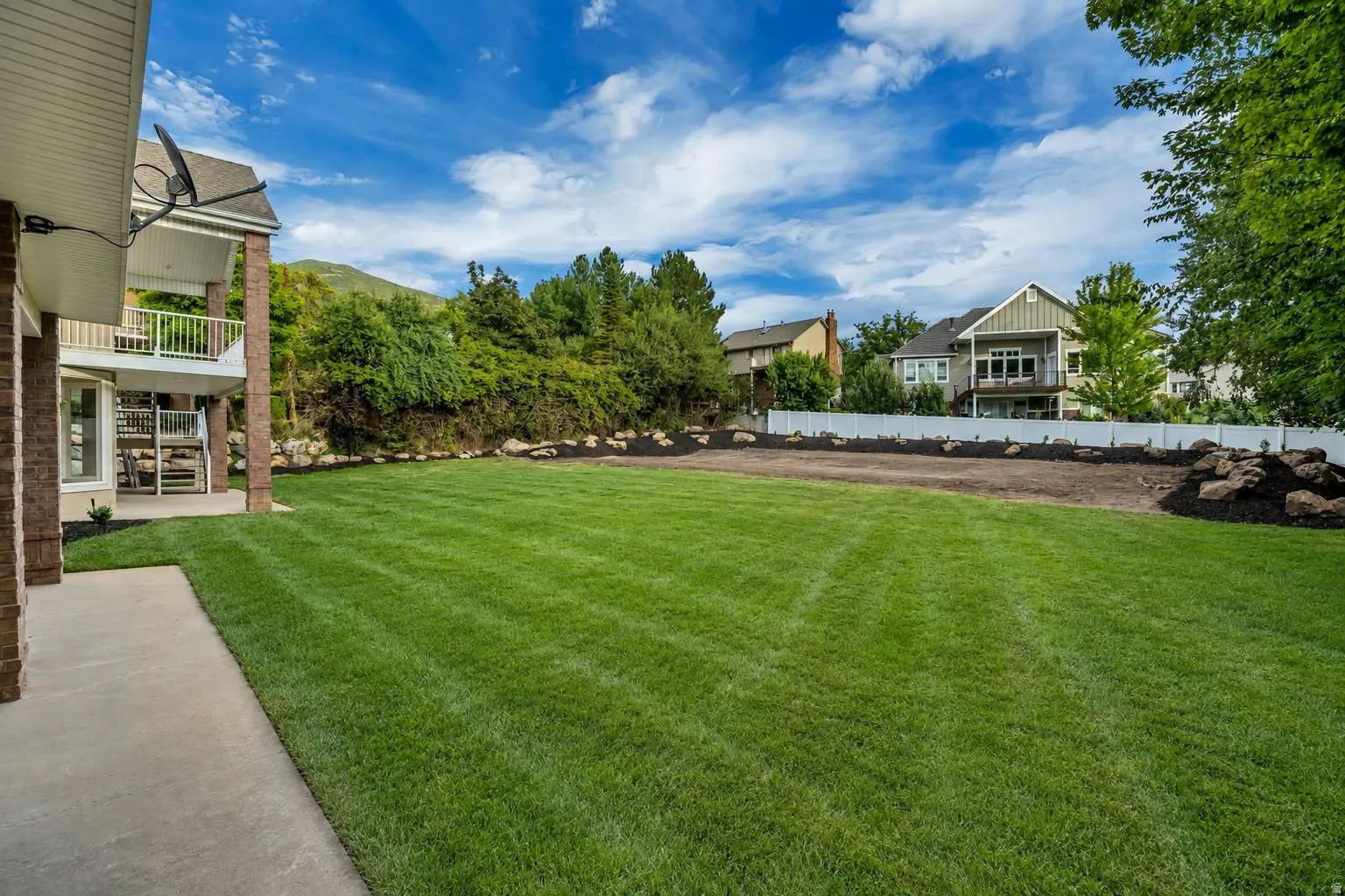 Expansive green lawn, concrete patio, multi-level decks, brick support columns, and privacy fencing