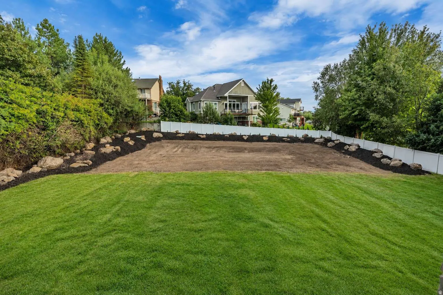 Expansive backyard with a manicured lawn, a level graded area, and a white privacy fence