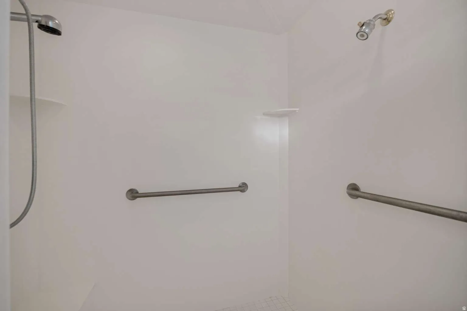 White shower enclosure with dual showerheads, built-in shelving, and grab bars