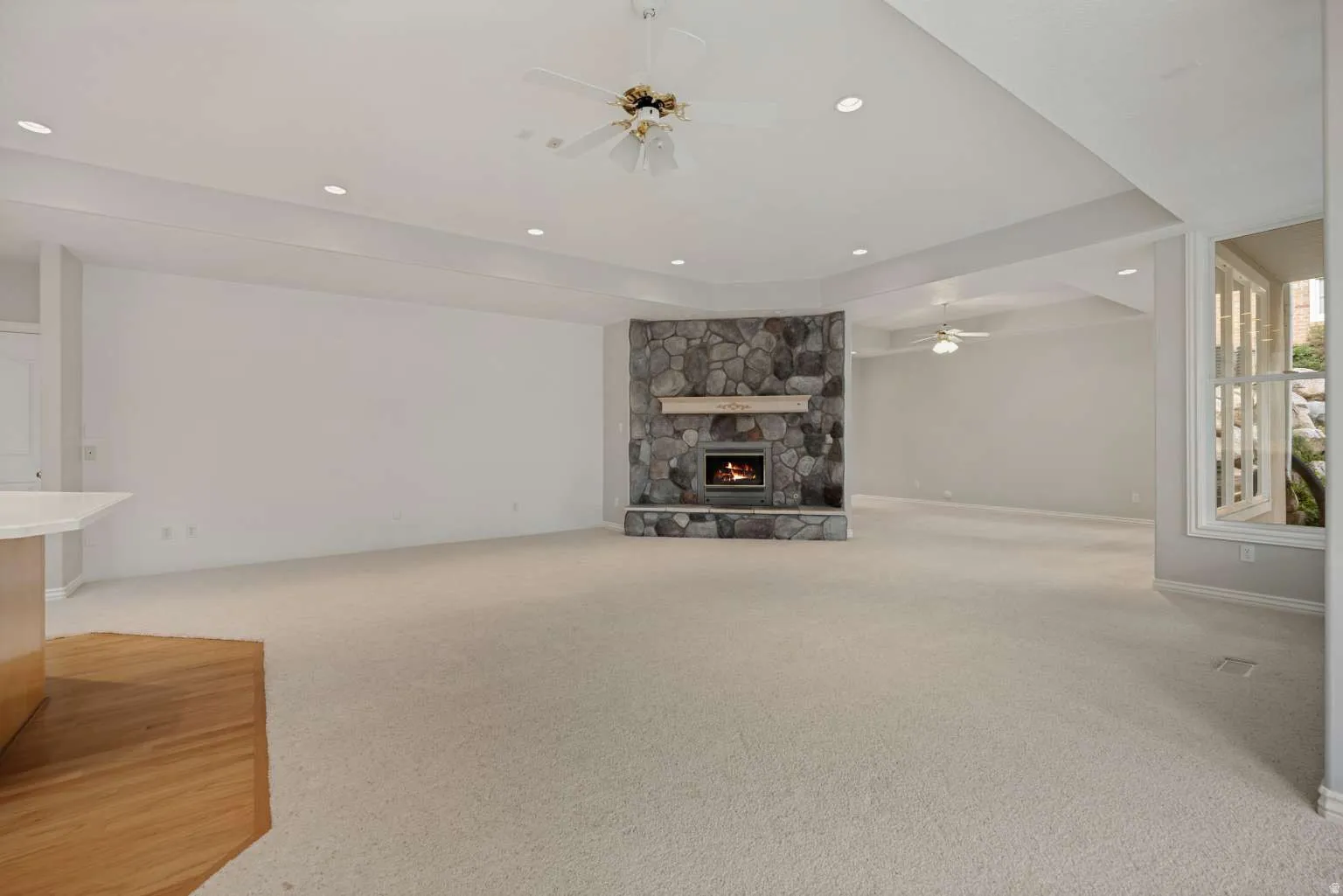 Stone-clad fireplace with a hearth, tray ceiling with recessed lighting, ceiling fan, and wood-finish flooring