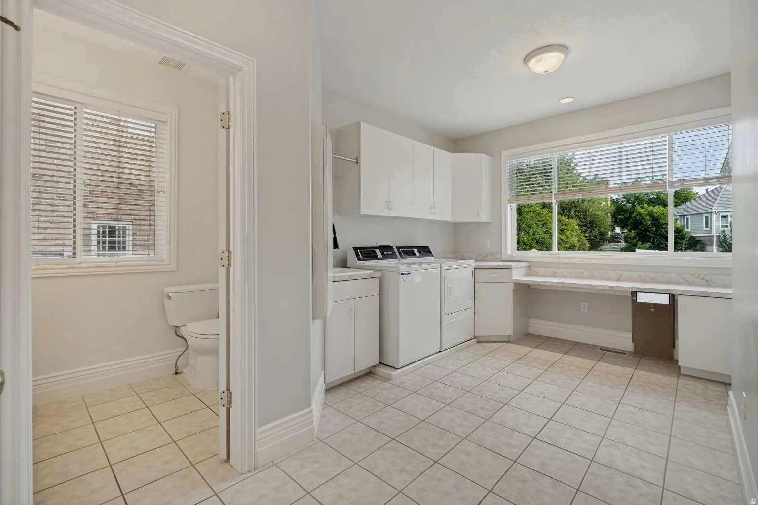 Spacious utility area featuring ceramic tile flooring, white cabinetry, a built-in countertop, and a large window