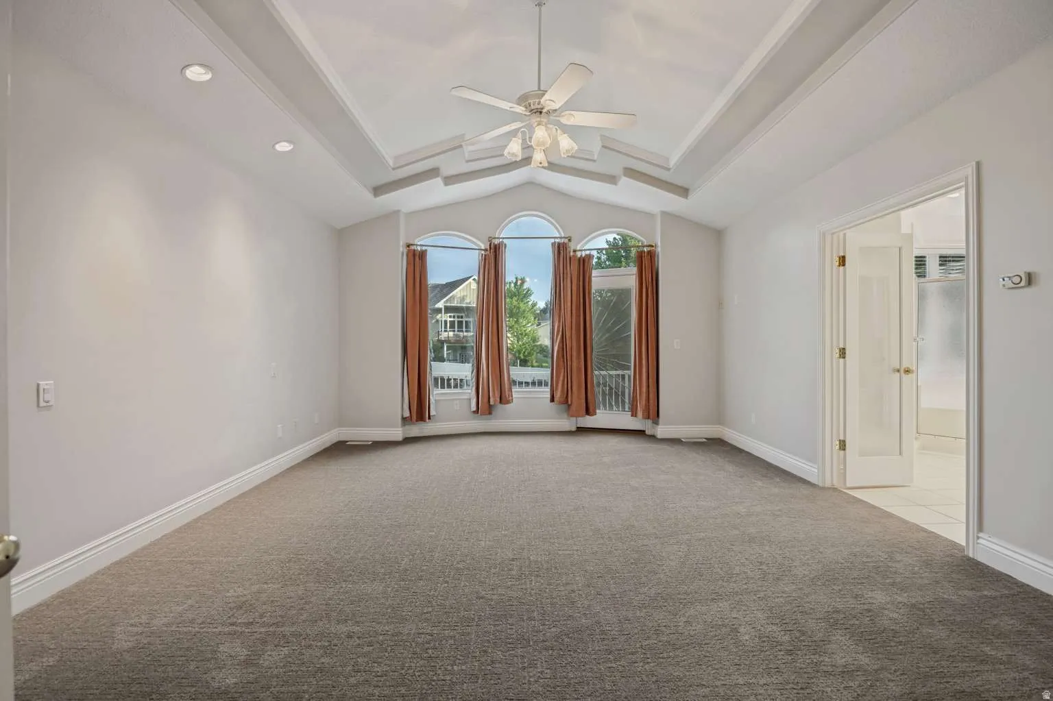 Tray ceiling with a ceiling fan, recessed lighting, arched windows, French doors, and an en-suite bathroom with tiled flooring