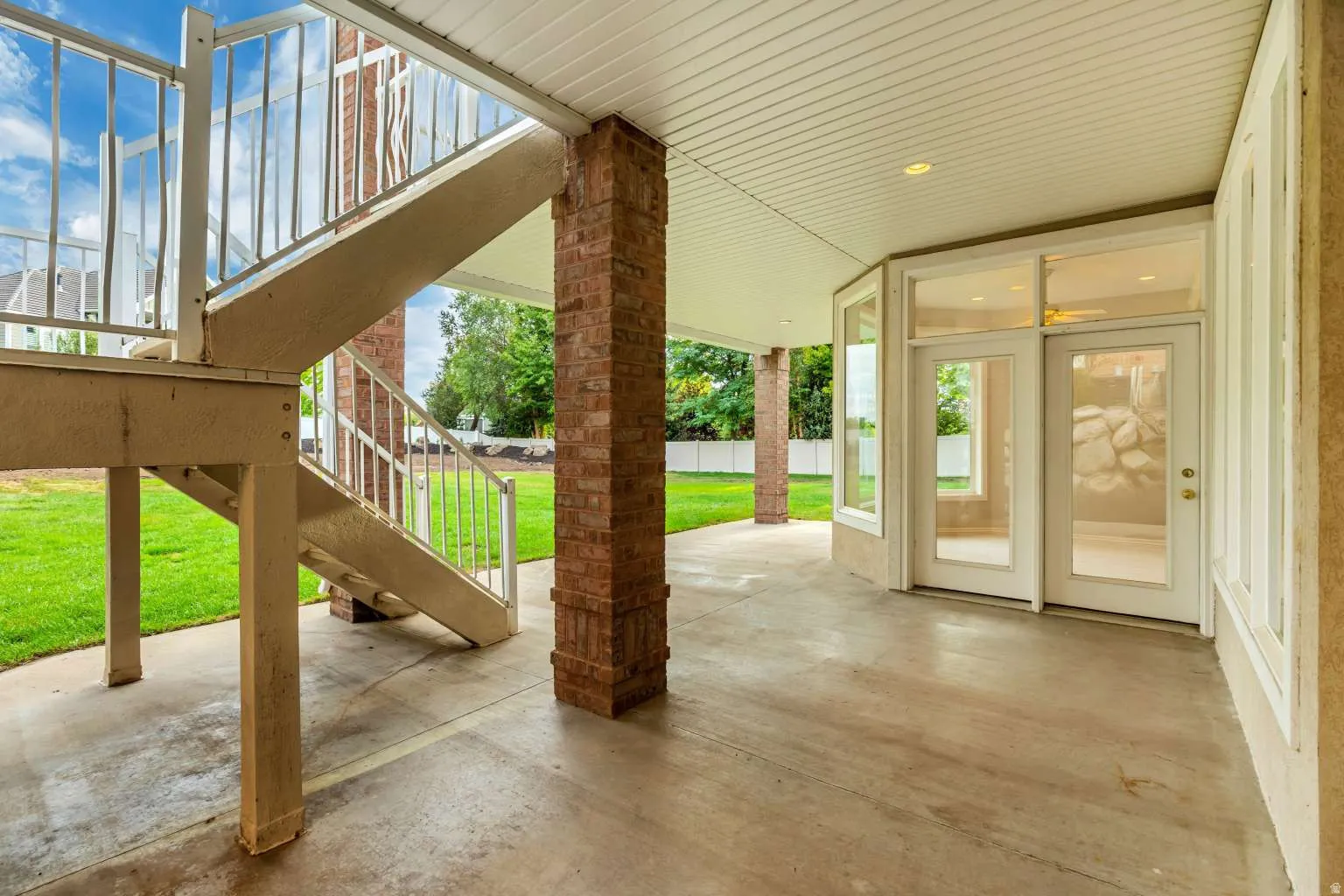 Covered patio with a concrete surface, brick support columns, and multiple glass-paneled doors