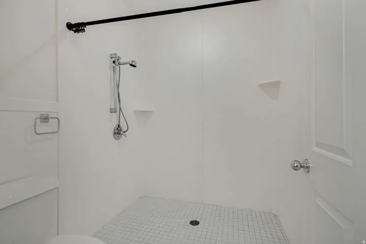 Shower with white panel walls, chrome fixtures, and white mosaic tile flooring
