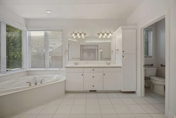 Recessed lighting, tile flooring, dual vanity with a large mirror, built-in soaking tub, and a tall built-in storage cabinet