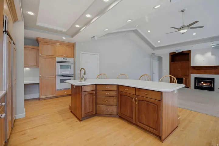 Kitchen island with integrated sink, wood-finish flooring, recessed lighting, and double wall ovens