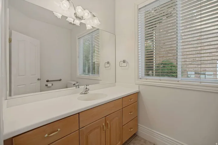 Bathroom with a single vanity, light wood cabinetry, white countertop, and a window with blinds