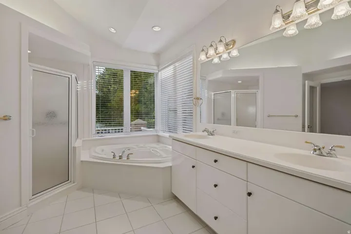 Dual vanity with integrated sinks, built-in corner jetted tub, enclosed shower, and tiled flooring