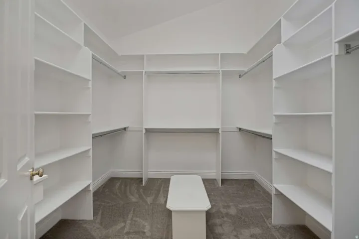 Expansive walk-in closet featuring extensive built-in shelving, multiple hanging rods, a central built-in bench, and carpeted flooring
