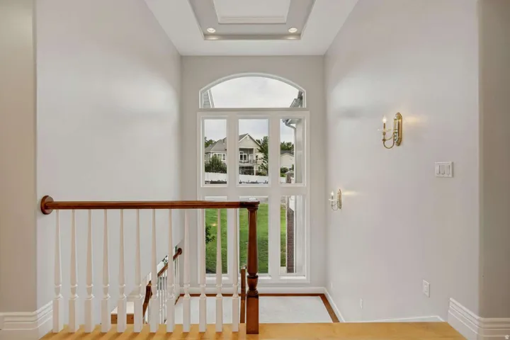 Arched window with multiple panes, recessed ceiling lighting, decorative wall sconces, wood-finish flooring, and a classic wood and white baluster staircase