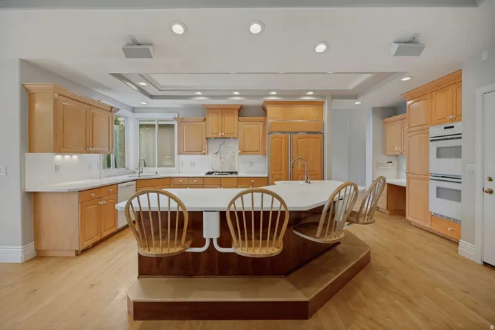 Spacious kitchen featuring light wood cabinetry, white countertops, built-in double ovens, a center island with seating, and recessed lighting