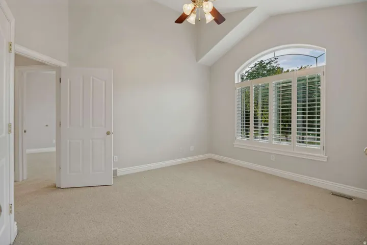 Vaulted ceiling room with an arched window, plantation shutters, and a ceiling fan