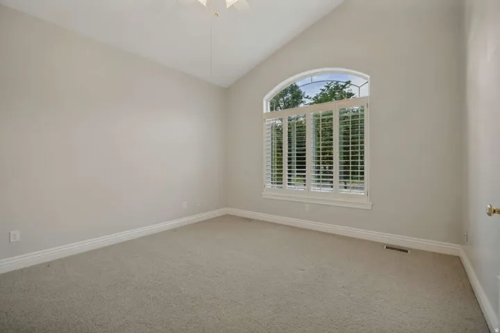 Vaulted ceiling with a ceiling fan, arched window with plantation shutters, and neutral carpeting