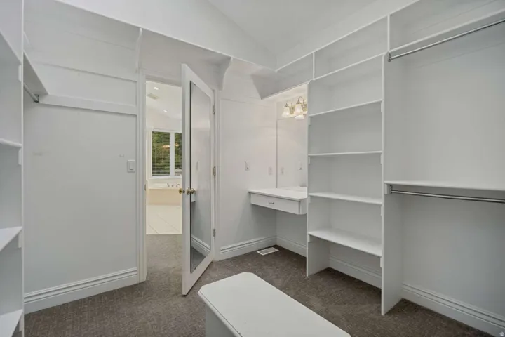 Built-in shelving, vanity desk with built-in drawer, garment rods, wall-mounted light fixture, and carpet flooring