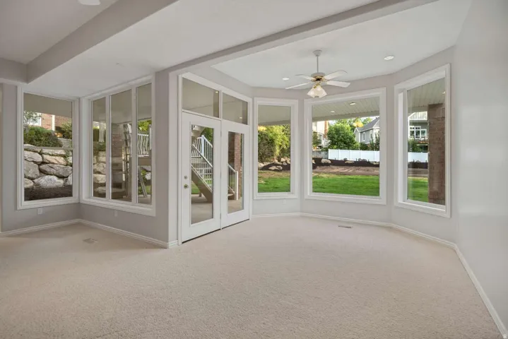 Wall-to-wall carpeting, extensive window placement, recessed lighting, ceiling fan, and double glass doors
