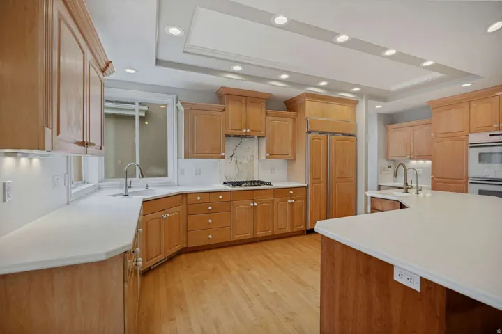 Kitchen featuring light wood cabinetry, light countertops, wood-finish flooring, a tray ceiling with recessed lighting, and integrated appliances