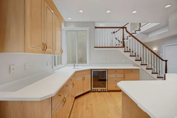 Wood-finish cabinetry with white countertops, integrated beverage cooler, and wood-finish flooring