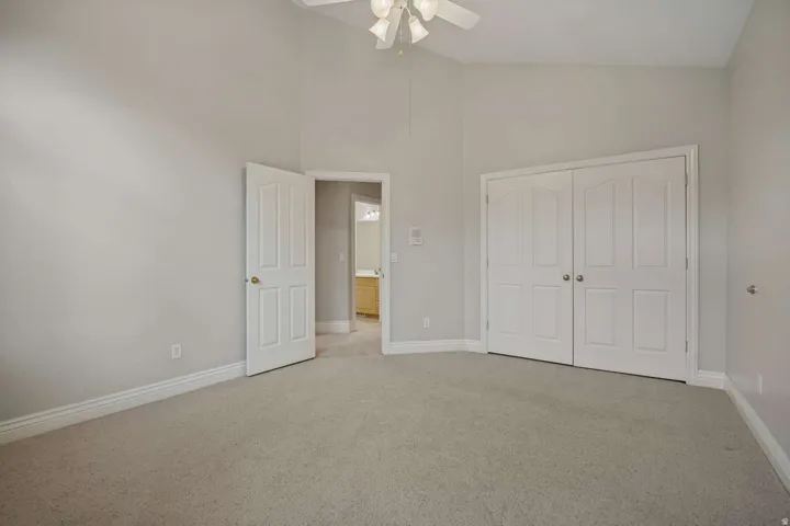 Vaulted ceiling with a ceiling fan, carpeted flooring, and bi-fold closet doors