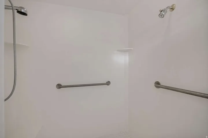 White shower enclosure with dual showerheads, built-in shelving, and grab bars
