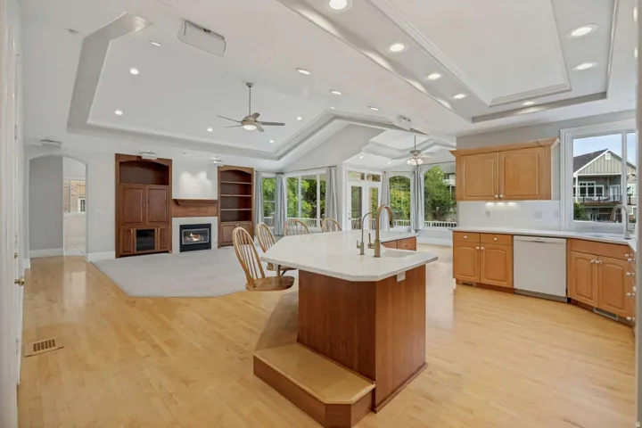 Open-concept living area with hardwood-finish flooring, a kitchen island with seating, a built-in fireplace with custom shelving, and a sunroom with large windows