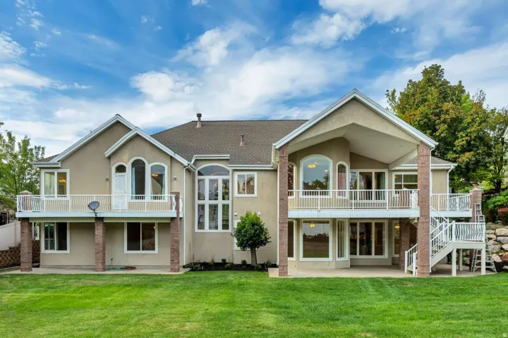 Multi-level stucco exterior with brick accents, expansive rear lawn, multiple walk-out balconies, and a covered patio