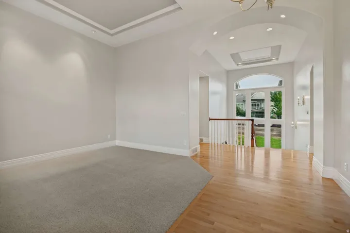 Tray ceiling with recessed lighting, wood-finish flooring, arched entryway, and spindle railing