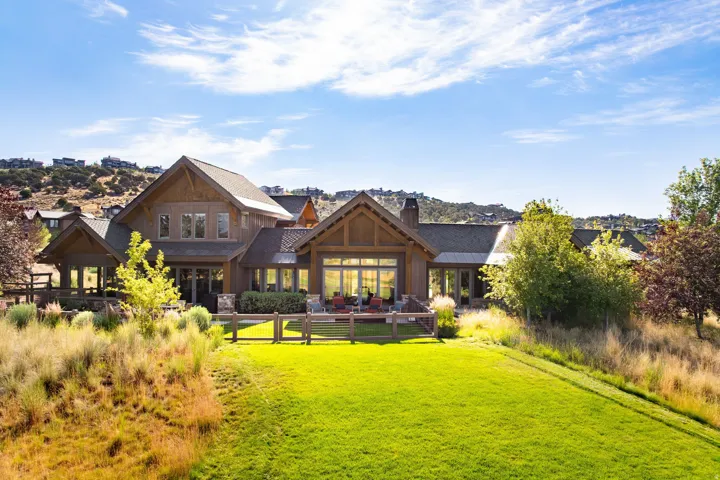 Expansive rear elevation featuring a multi-level wood-clad exterior, a gabled roofline, a spacious outdoor patio, a lush green lawn, and mature landscaping