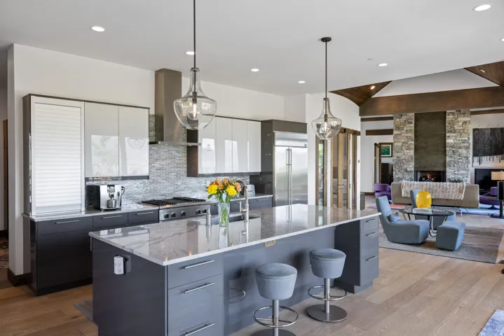 Modern kitchen featuring an expansive island with a light-toned countertop, stainless steel appliances, a mosaic tile backsplash, wood-finish flooring, and recessed lighting