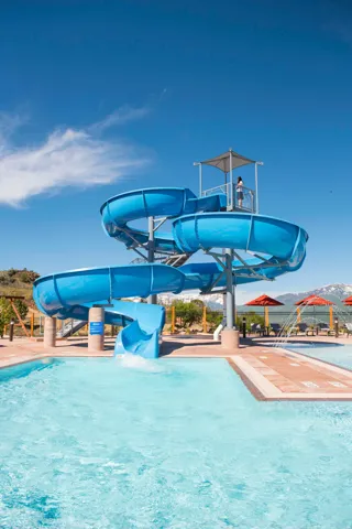 Multi-level blue waterslide emptying into a swimming pool with a concrete and tile surround