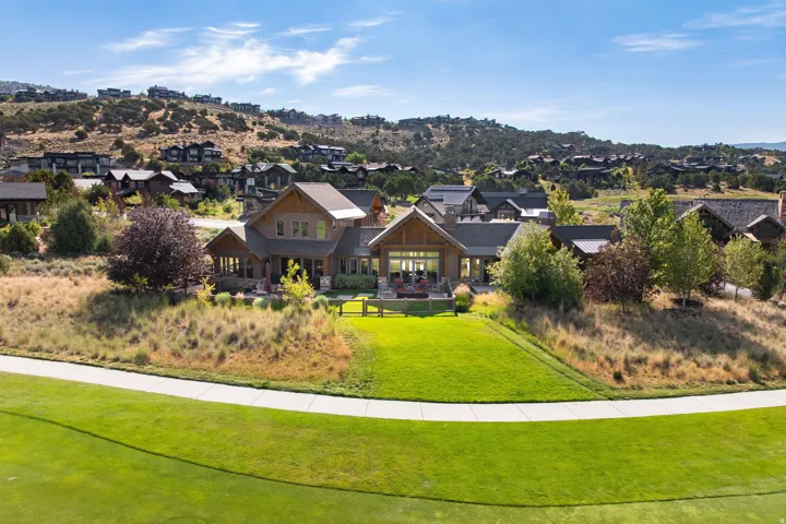 Expansive property featuring a multi-level residence with a covered patio, a manicured lawn, and natural landscaping, all set against a mountainous backdrop