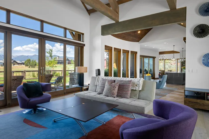 Spacious living area featuring exposed wood ceiling beams, floor-to-ceiling glass sliding doors, and light wood-finish flooring