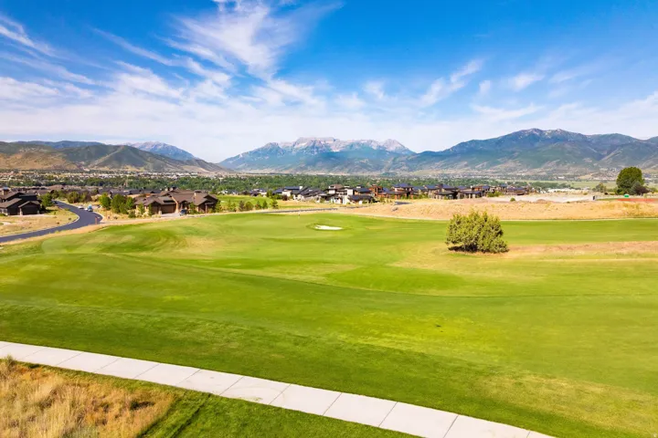 Expansive golf course green with a paved walking path and a scattering of mature trees