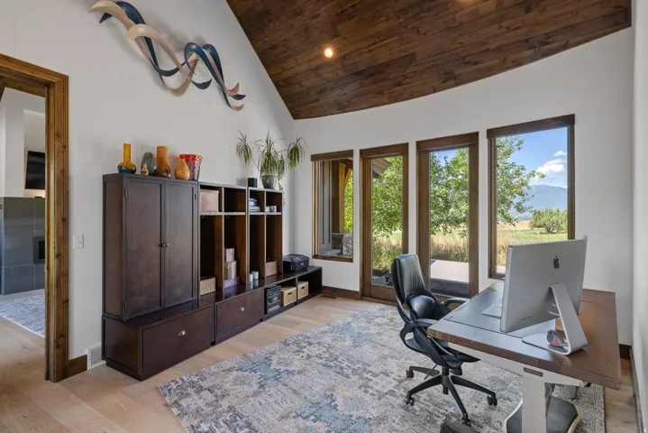 Room featuring a vaulted wood-paneled ceiling, light wood-finish flooring, built-in dark wood cabinetry, and multiple large windows with exterior access