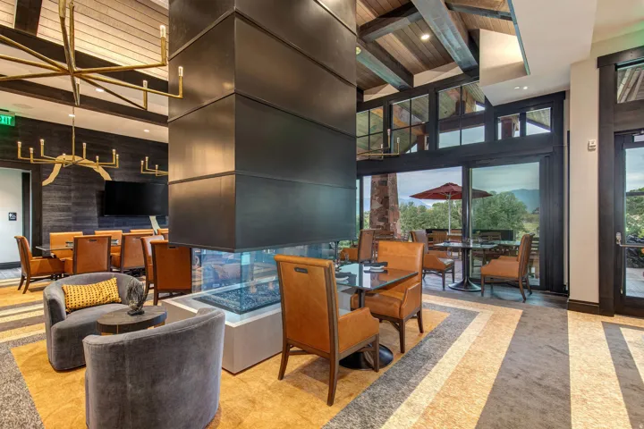 Central fireplace with glass viewing panels, vaulted wood-plank ceilings, expansive windows, glass patio doors, and a decorative chandelier