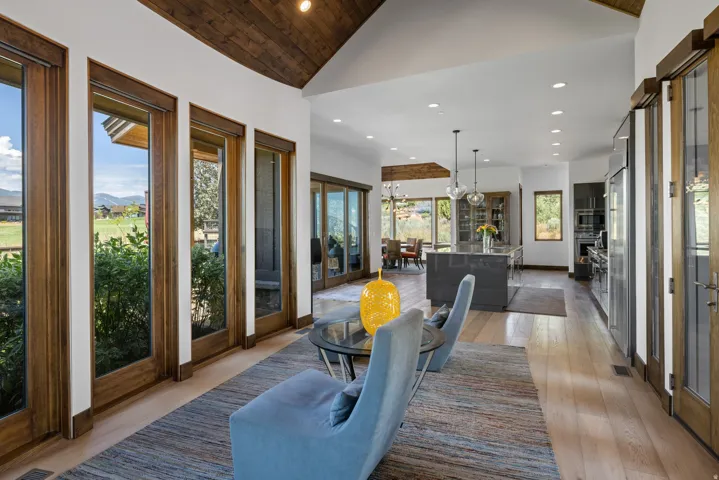 Spacious living area featuring a vaulted wood-finish ceiling, light wood-finish flooring, and multiple floor-to-ceiling windows with wood frames
