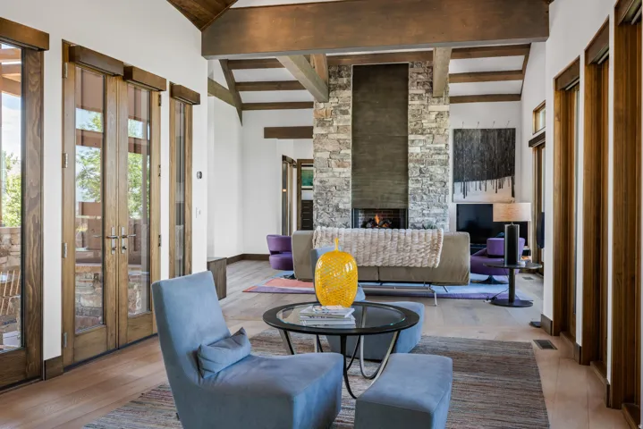 Spacious living area featuring exposed wood beams, a stone-clad fireplace with a dark-toned hearth, and wood-finish flooring