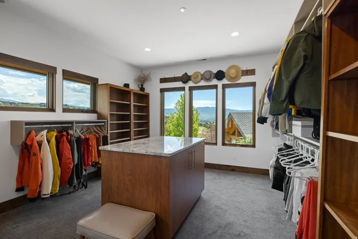 Walk-in closet featuring a central island with a light-toned countertop, built-in shelving, ample hanging storage, multiple windows, and recessed lighting