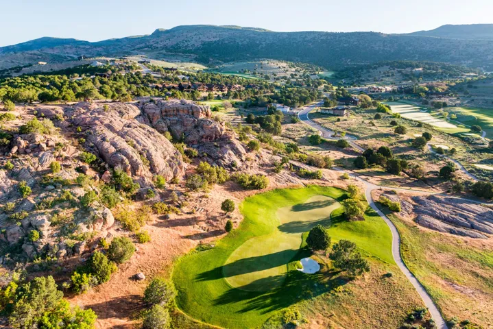Expansive golf course terrain featuring manicured greens, natural rock formations, mature trees, and winding cart paths