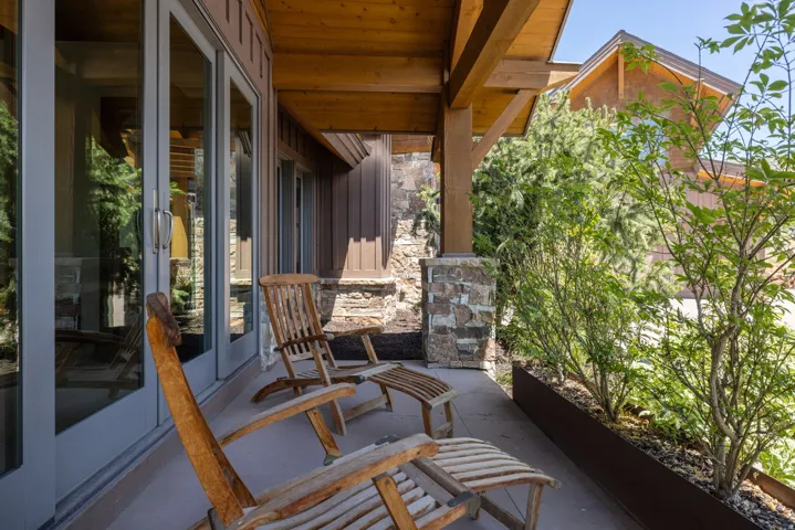 Covered patio with exposed wood beam ceiling, stone column accents, planter box landscaping, and multiple glass panel doors