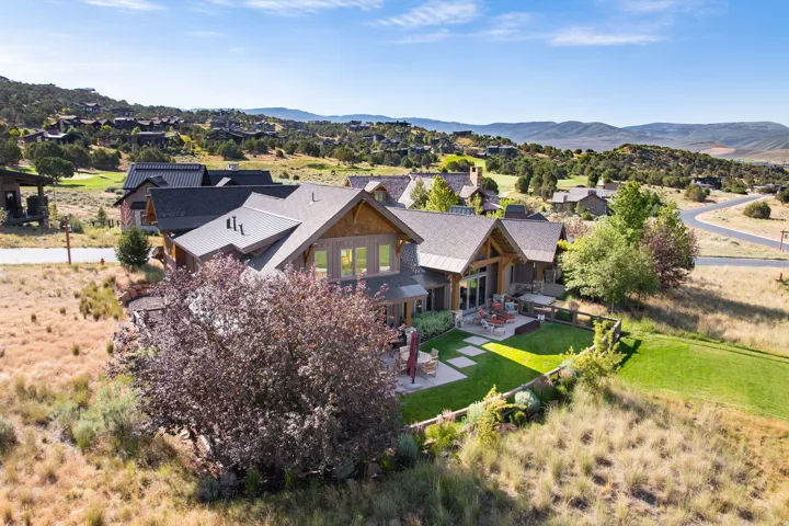 Expansive property featuring a stone and wood siding exterior, multiple gabled roofs, a manicured lawn, and a stone patio