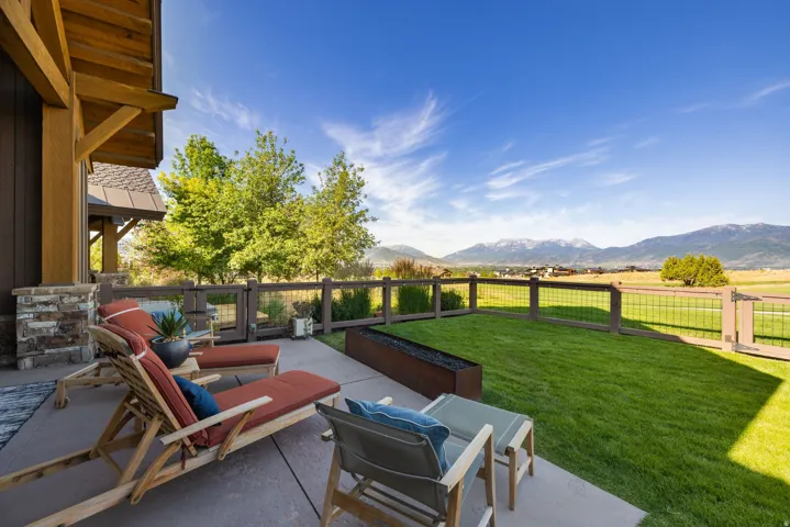 Spacious concrete patio featuring a low-profile fire pit, a perimeter fence, and a generous lawn area