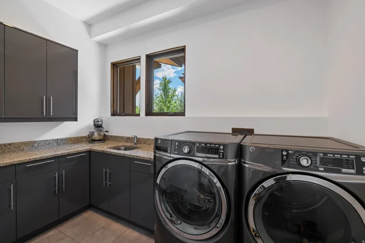 Laundry area featuring built-in cabinetry, stone-finish countertops, an undermount sink, and two windows