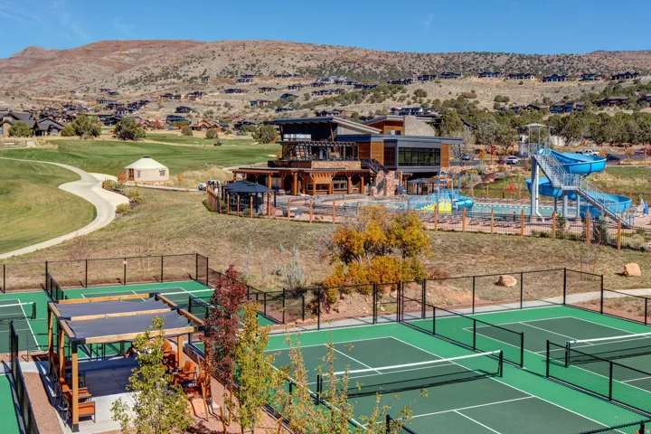 Outdoor recreational area featuring multiple tennis courts, a shaded seating area with a pergola, a multi-level clubhouse, a swimming pool with water slides, and a golf course