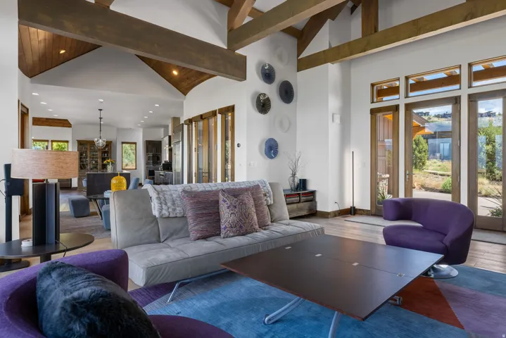Vaulted ceilings with exposed wood beams, hardwood flooring, and multiple glass-paned doors opening to the exterior