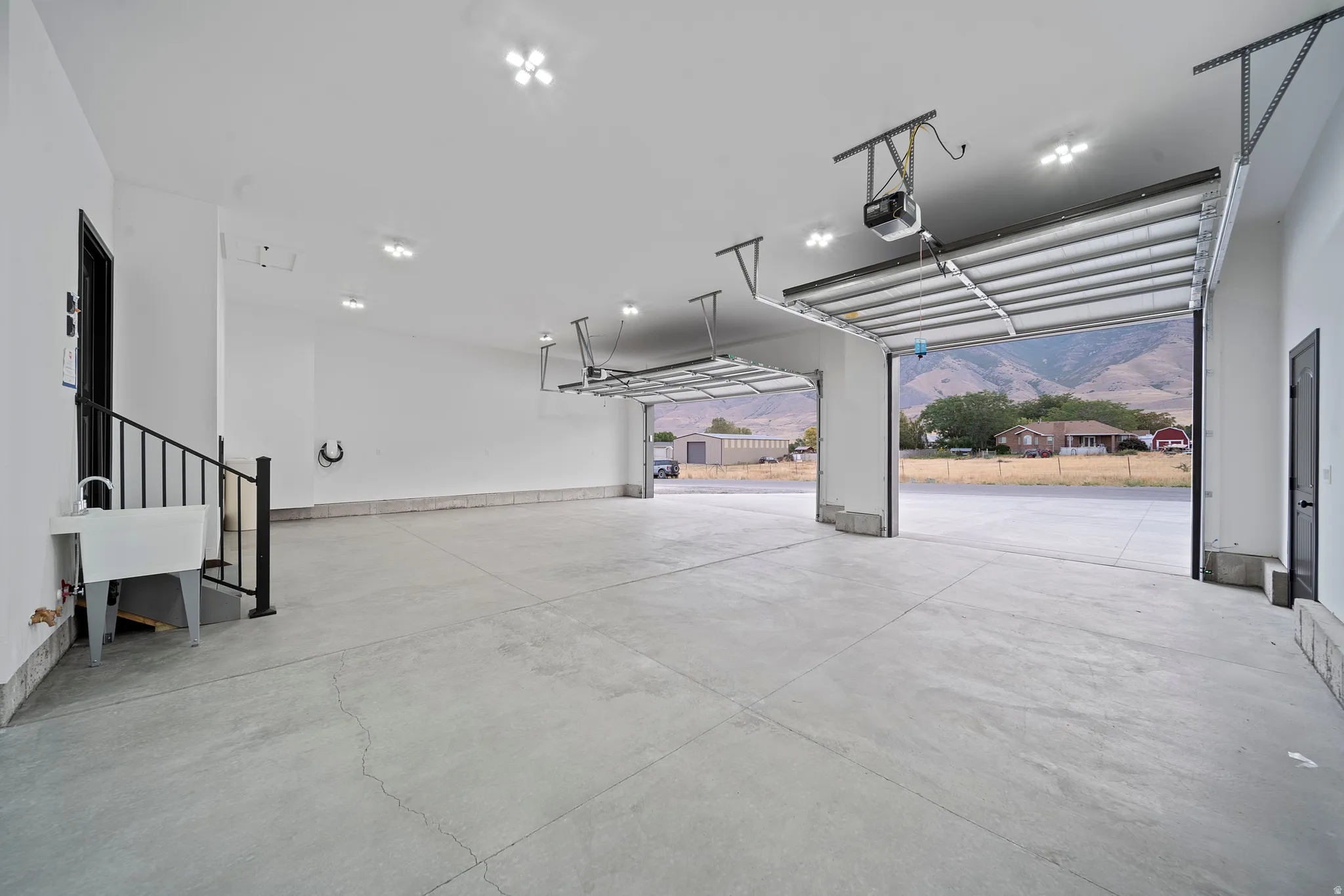 Spacious garage featuring concrete flooring, multiple overhead garage doors, an integrated utility sink, and built-in ceiling lighting
