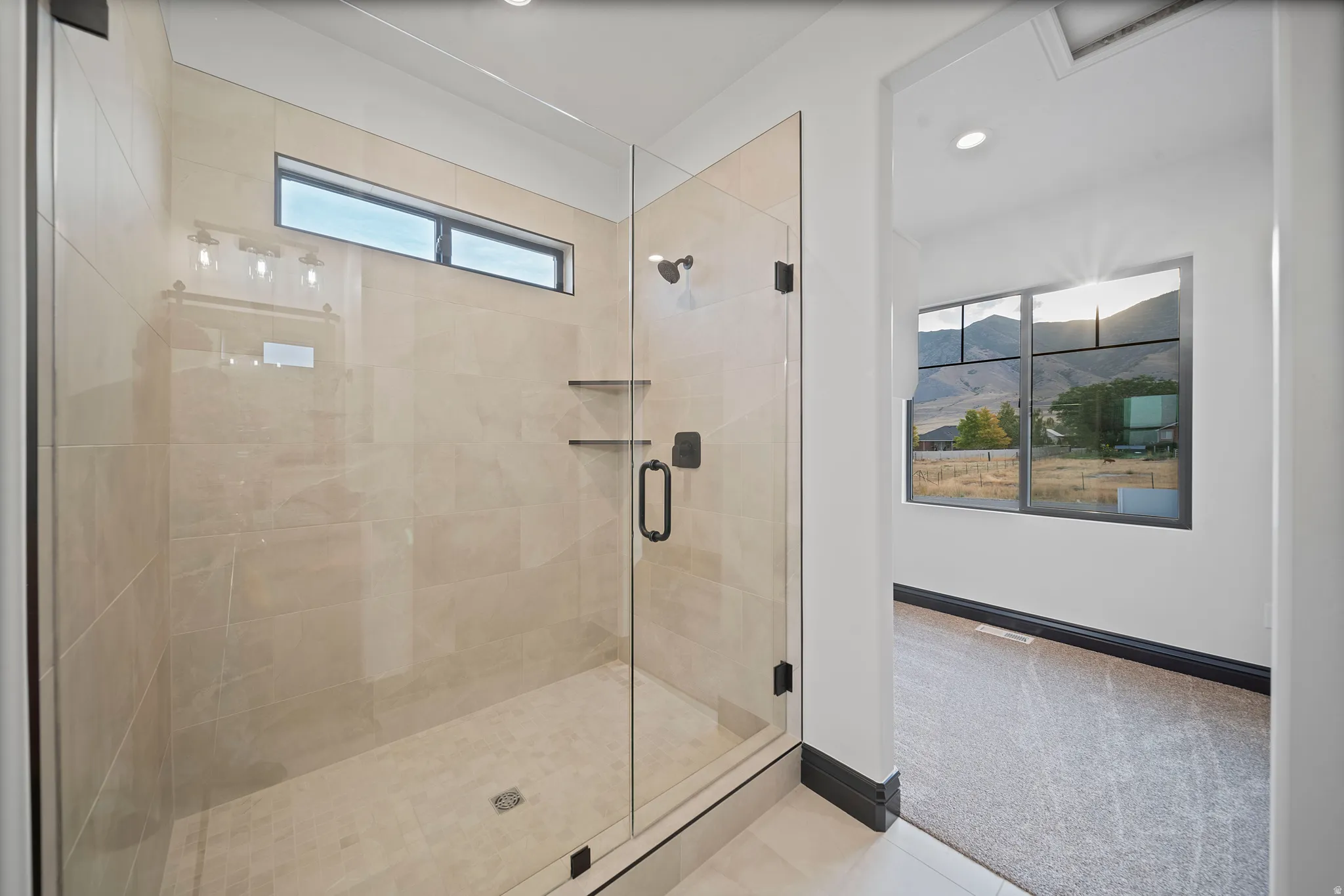 Spacious shower enclosure with floor-to-ceiling glass, light-toned tile surround, built-in shelving, and transom window