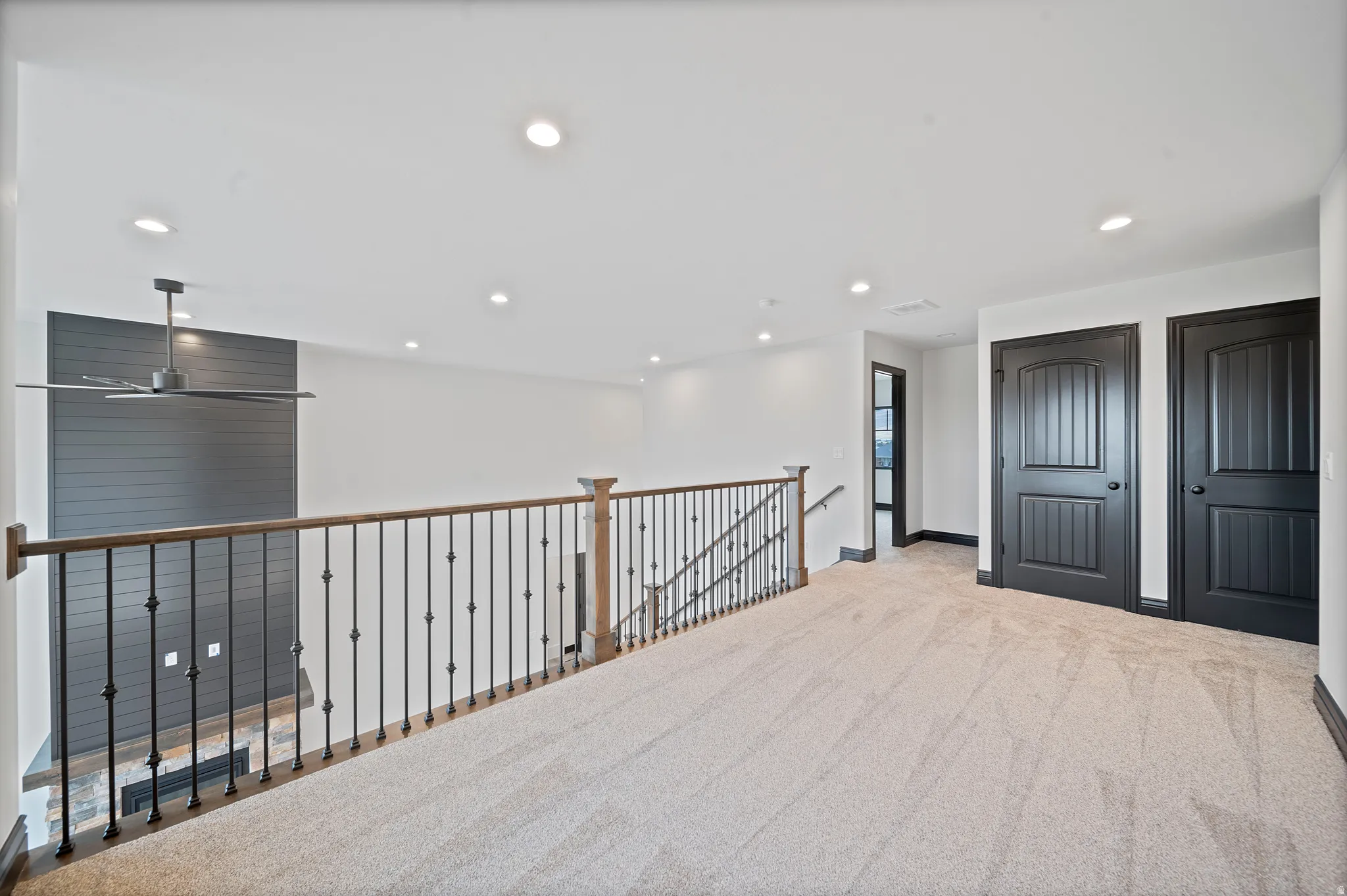 Spacious upper-level landing with neutral carpeting, recessed lighting, and a modern ceiling fan